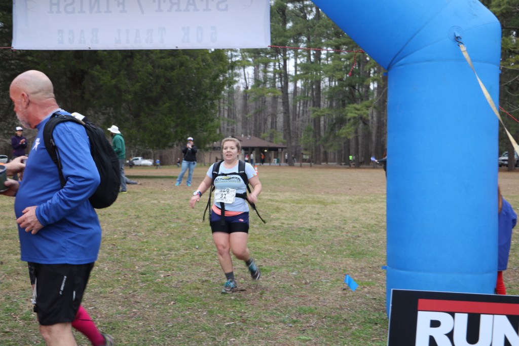 Female runner about to cross the finish arch of the Algonquin 50K, with a man to the left.