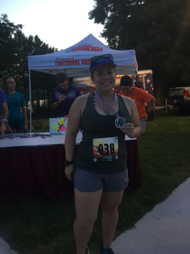 Vanessa Junkin wearing running clothes and standing with medal around neck and holding it. A tent is in the background. 