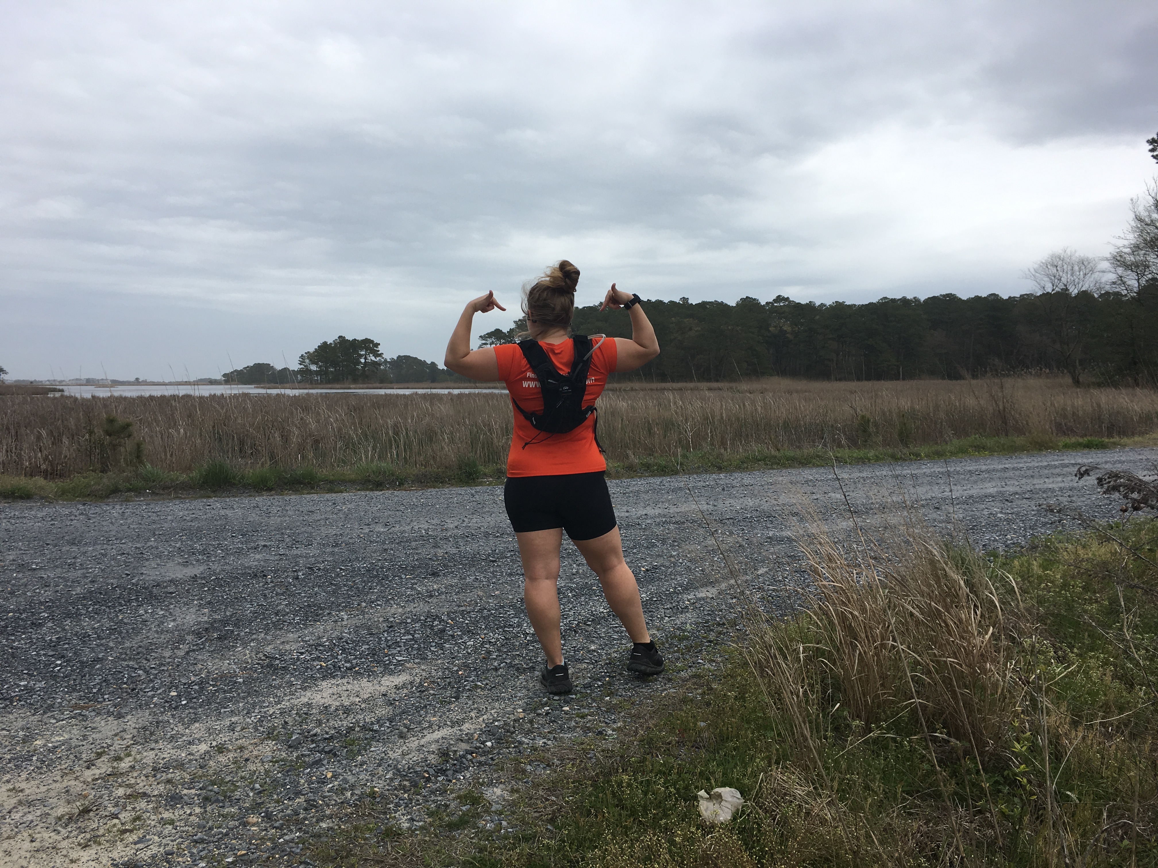 Vanessa Junkin, facing away from the camera, shows the Orange Mud Gear Vest Pro on a gravel road at the Assawoman Wildlife Area.