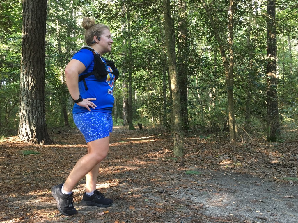 Vanessa Junkin wearing the AfterShokz Aeropex (view from the side) standing on a wooded trail. 
