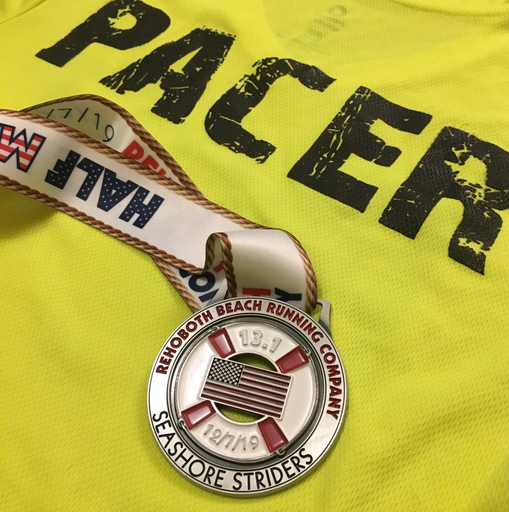 Rehoboth Beach Seashore Half Marathon medal with the backdrop of a yellow shirt that says "PACER." 