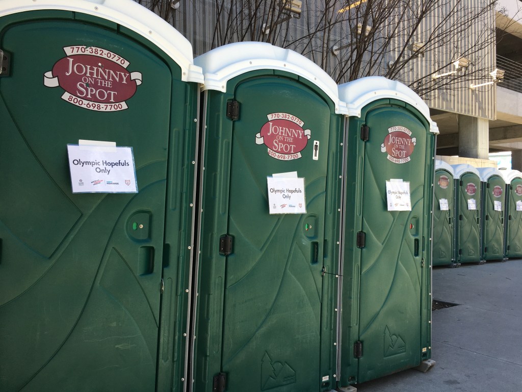 Line of green porta-potties with "Olympic Hopefuls Only" signs on them. 