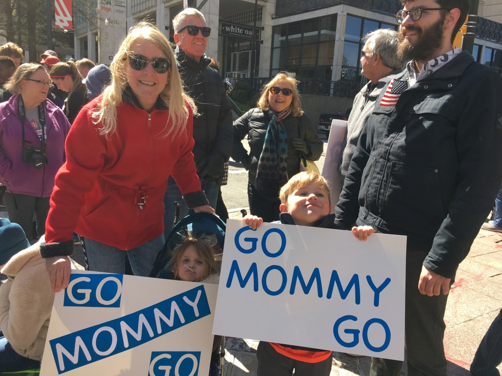 Keira D'Amato's family members hold signs that read "Go Mommy Go." 