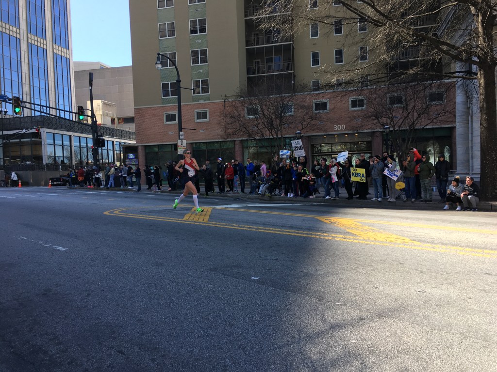 Keira D'Amato runs past a crowd. Some are holding signs.