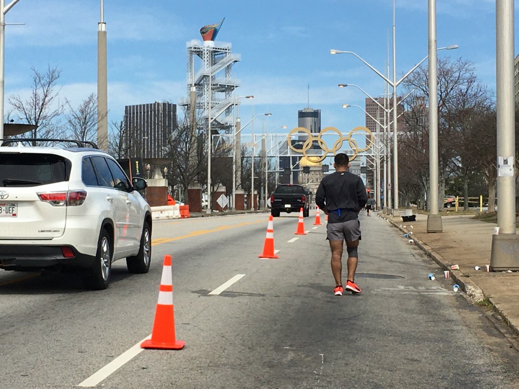 Gold Olympic rings and the Olympic cauldron are shown, with a runner in front of where the photo is being taken, too.