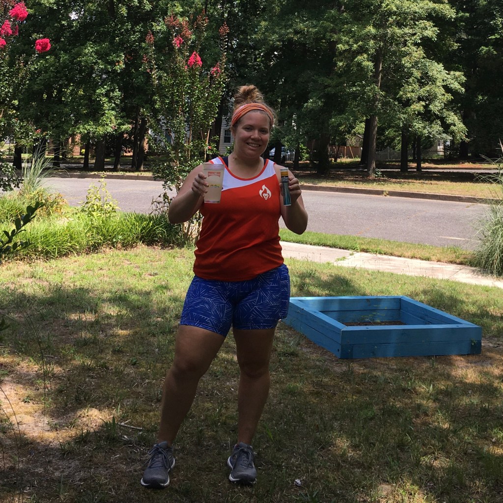 Vanessa Junkin standing outside holding a pint glass with liquid in it and a tube of the Science in Sport GO Hydro tablets. 