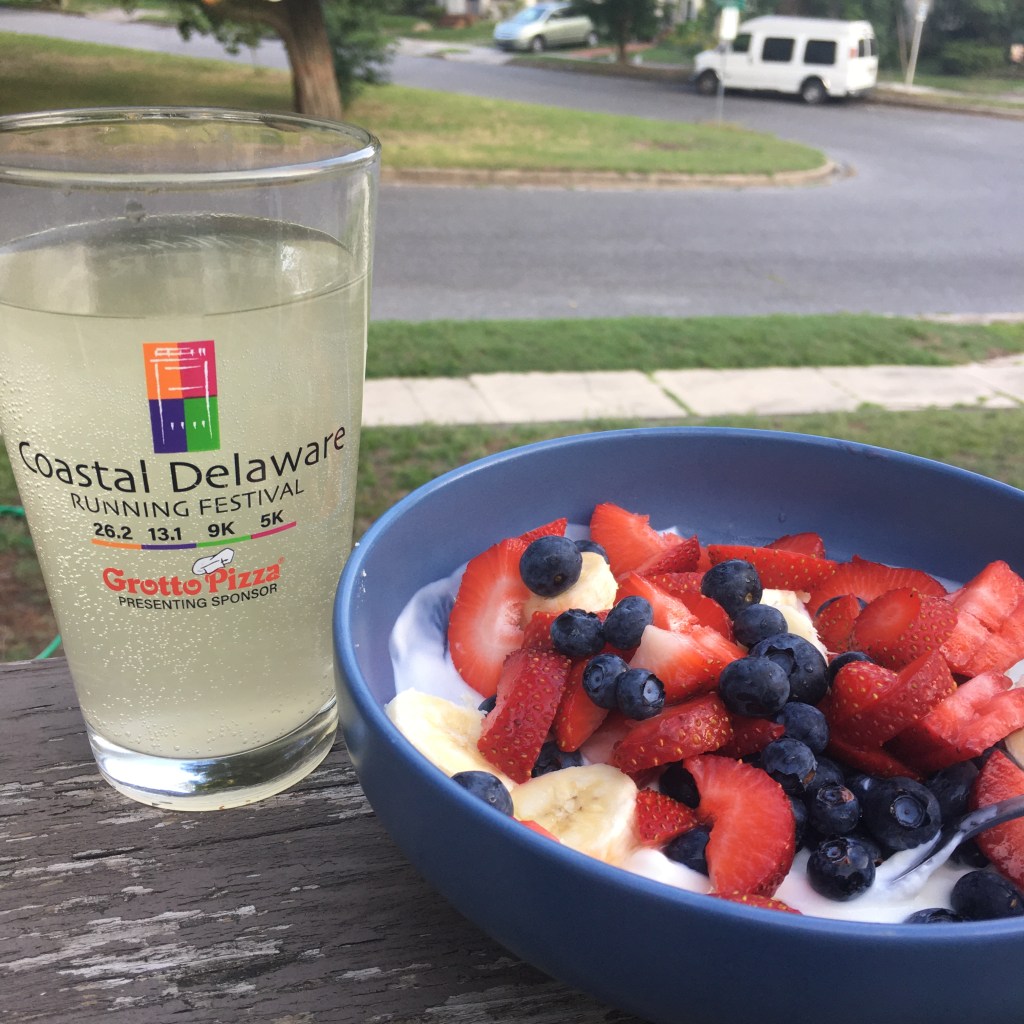 Pint glass with very pale yellow drink (Science in Sport GO Hydro Pineapple & Mango) and a blue bowl with strawberries, blueberries, bananas and yogurt in it. 