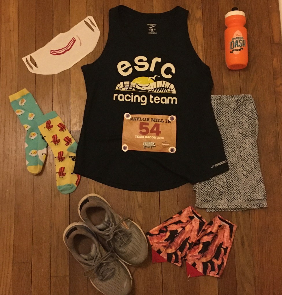 A flat lay photo showing a mask with an image of bacon on it, an ESRC Racing Team tank top with a race bib on it, socks with eggs on one and bacon on the other, running shorts, running shoes and bacon gaiters. 