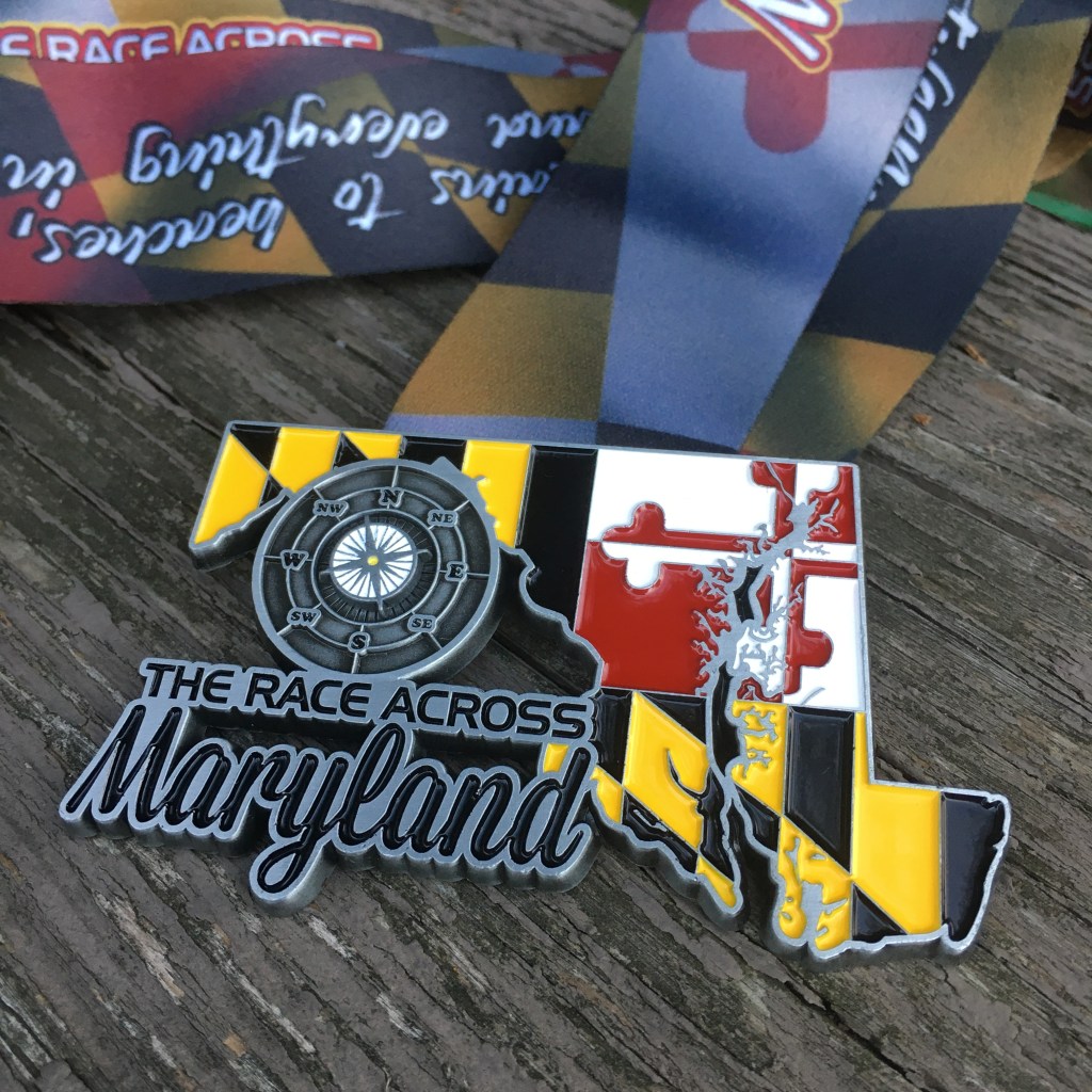 Race Across Maryland medal, which is in the shape of Maryland with the Maryland flag design on it. It says "The Race Across Maryland" and has a compass. 