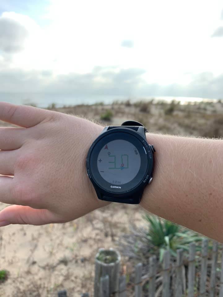 View of watch showing a route in the shape of a "30" on wrist in front of a blurred beach background. 
