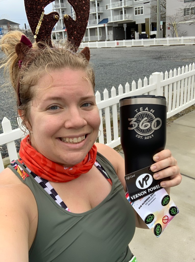 Female runner holding a large black tumbler with TEAM 360 logo, a VP Shoes gift card and TEAM 360 BibBoards. 