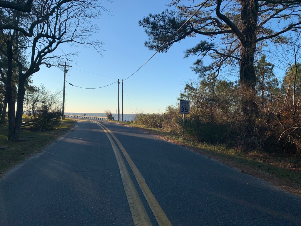 Photo of a road with water in the distance on the right. 