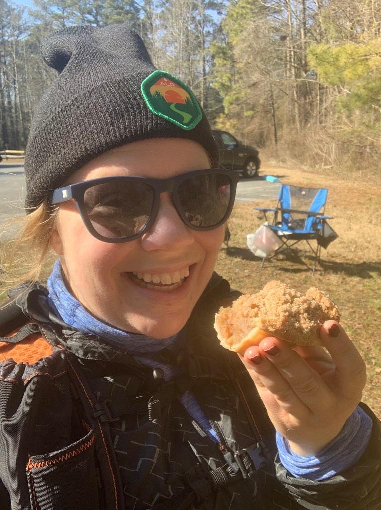 Selfie of female runner in hat and sunglasses with pie in her hand. 