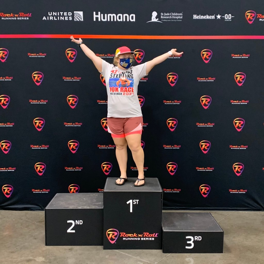 Vanessa Junkin poses with arms up on podium photo op at the Rock 'n' Roll Virginia Beach expo. 