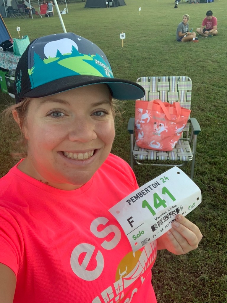 Selfie of Vanessa Junkin holding race bib with chair and bag in the background. 