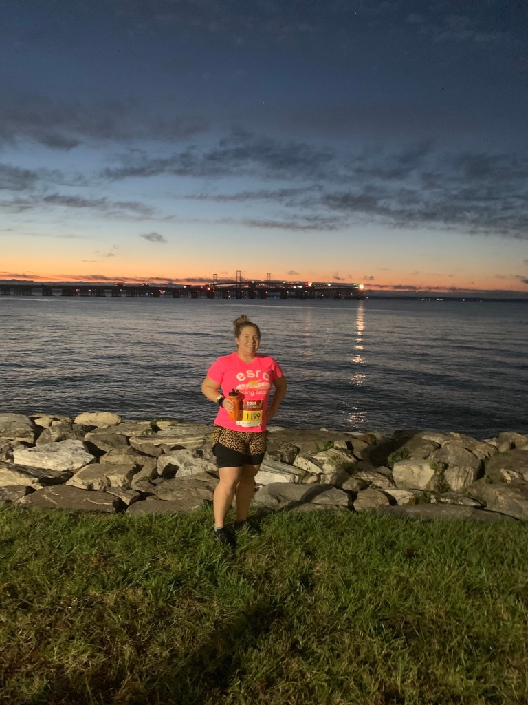 Vanessa Junkin stands against backdrop with water, sunrise and bridge. 