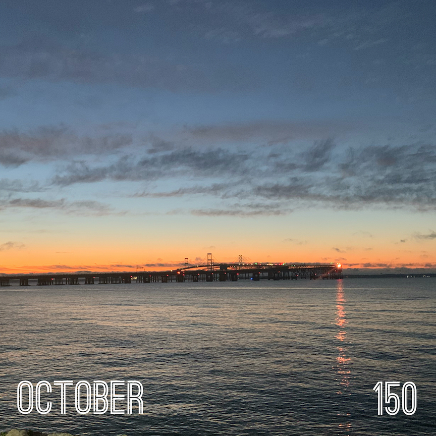 View of the Chesapeake Bay Bridge at sunrise with the bay in the foreground of the photo. Text reads "October" and "150."