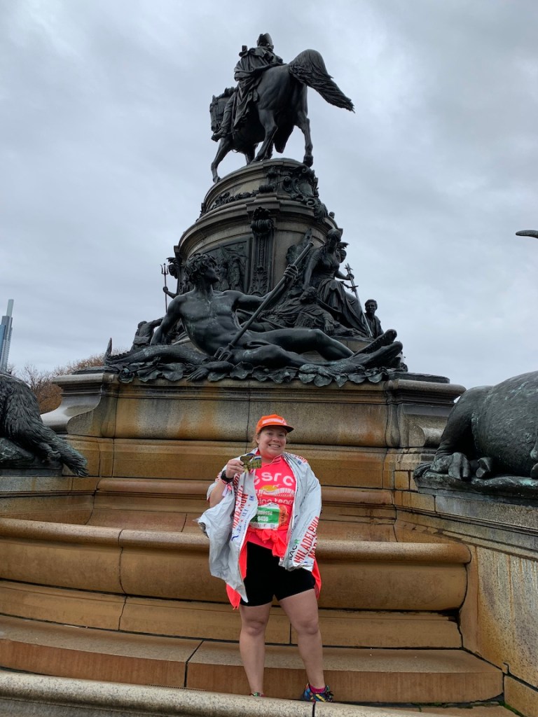 Vanessa Junkin poses with her medal in front of a fountain with a statue after the Philadelphia Marathon. 