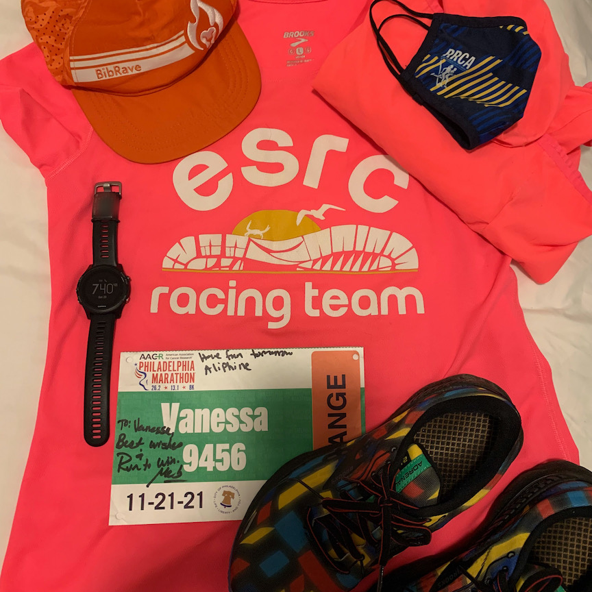 Running items laid out for a photo, including ESRC Racing Team shirt, signed race bib, watch, shoes, jacket, hat and mask.