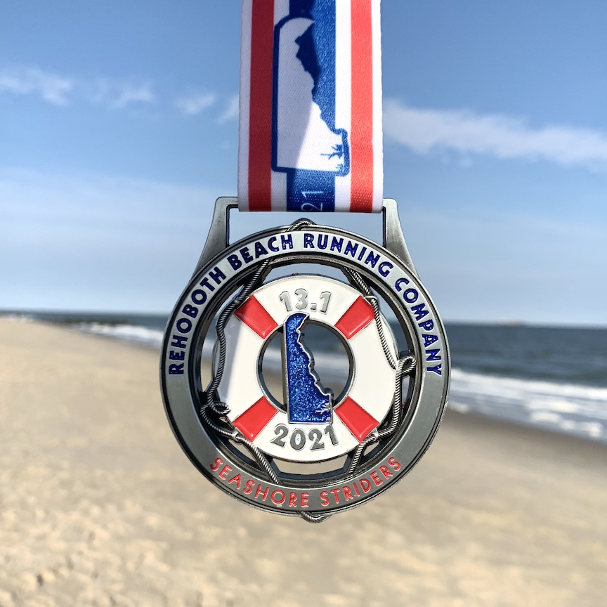 Rehoboth Seashore Half Marathon medal in front of the beach. 