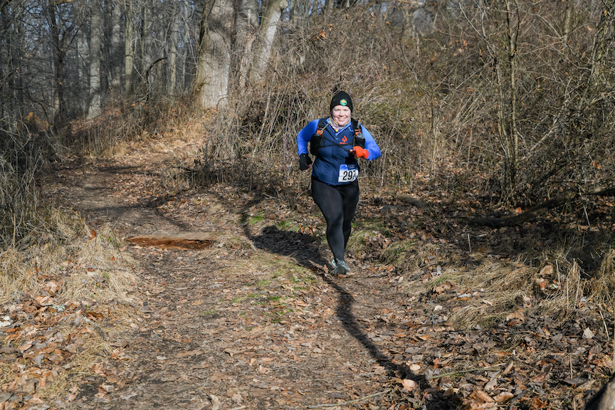 Female runner, bundled up and running on wooded trail in the winter. 
