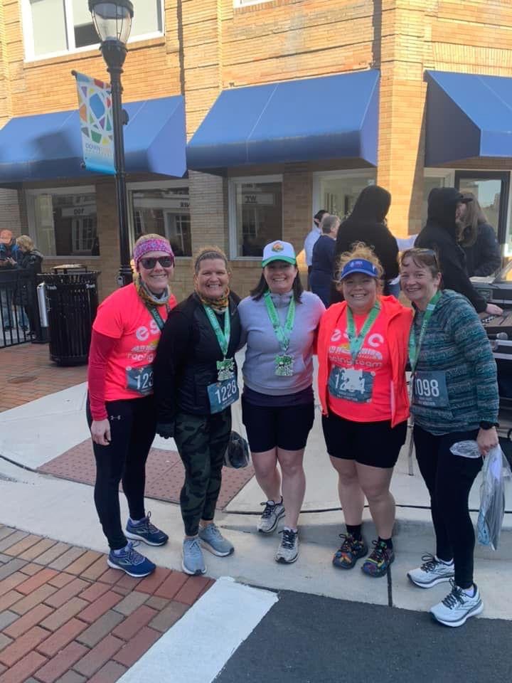 Group of five smiling female runners wearing medals. 