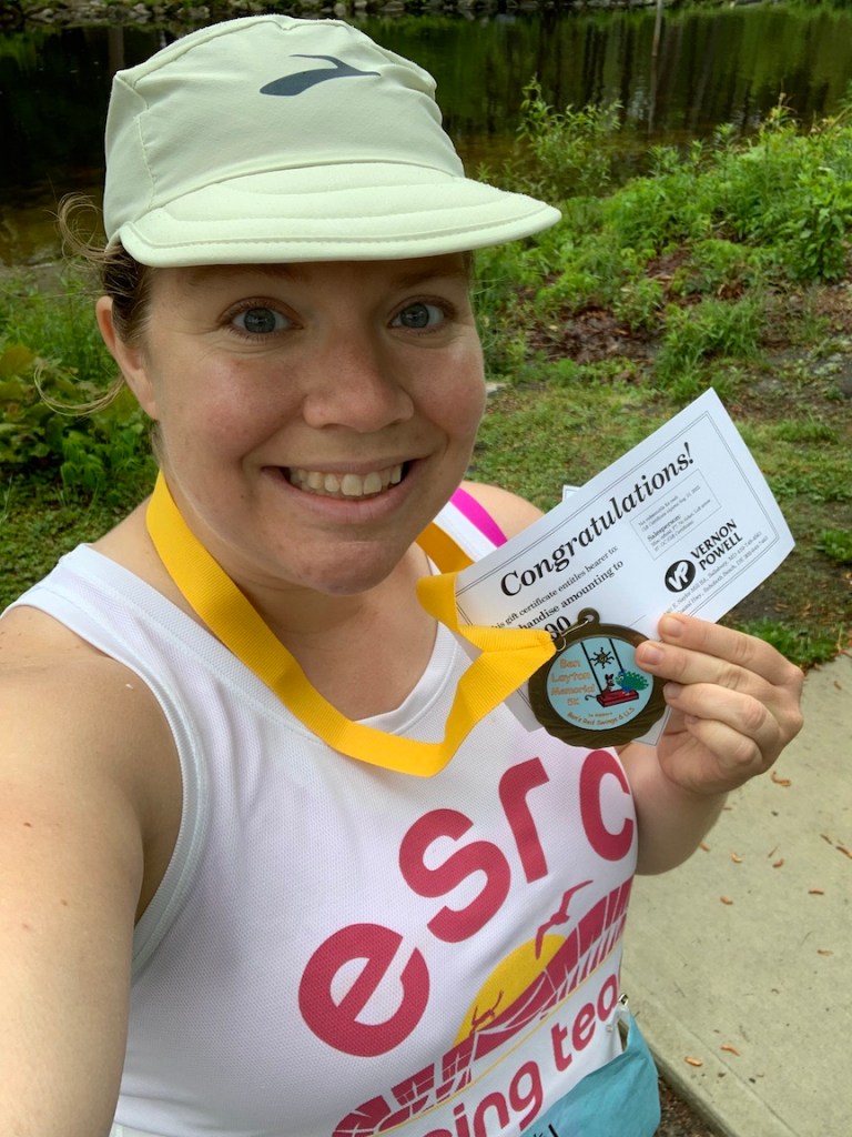 Selfie of Vanessa Junkin holding race medal and gift certiicate to VP Shoes. 
