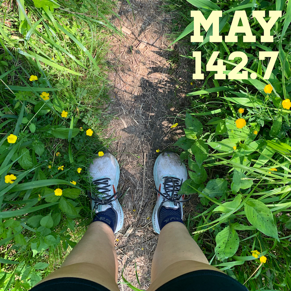 Photo of legs/feet in running shoes on a thin trail with plants and flowers on both sides with the text "May 142.7." 
