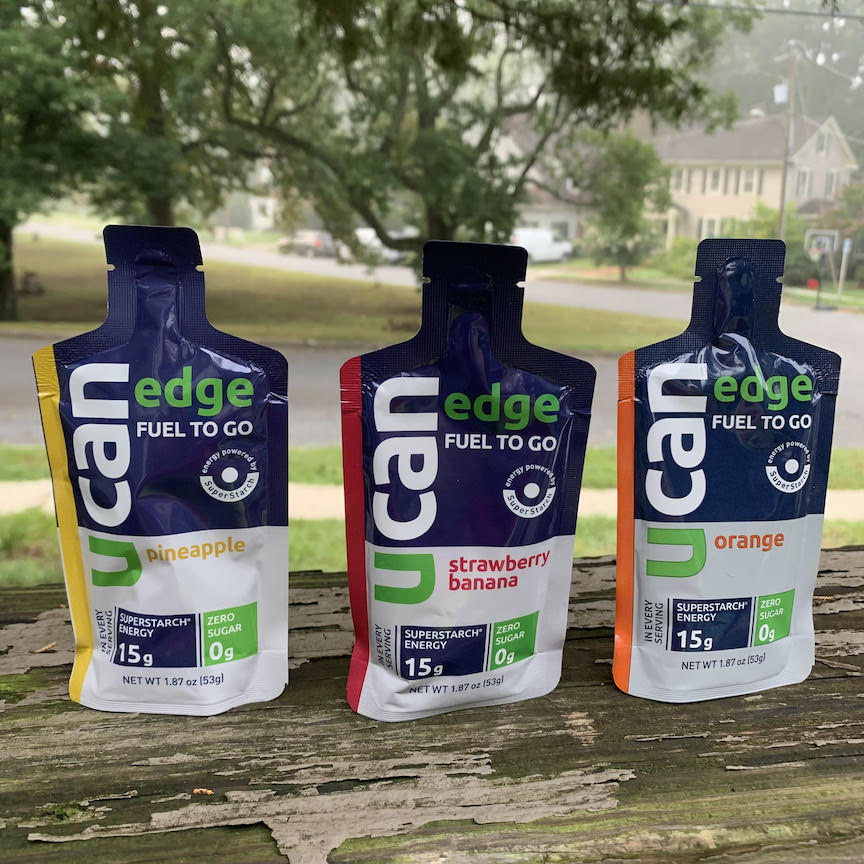 Three UCAN Edge gels are set up on a wooden rail — Pineapple, Strawberry Banana and Orange. 