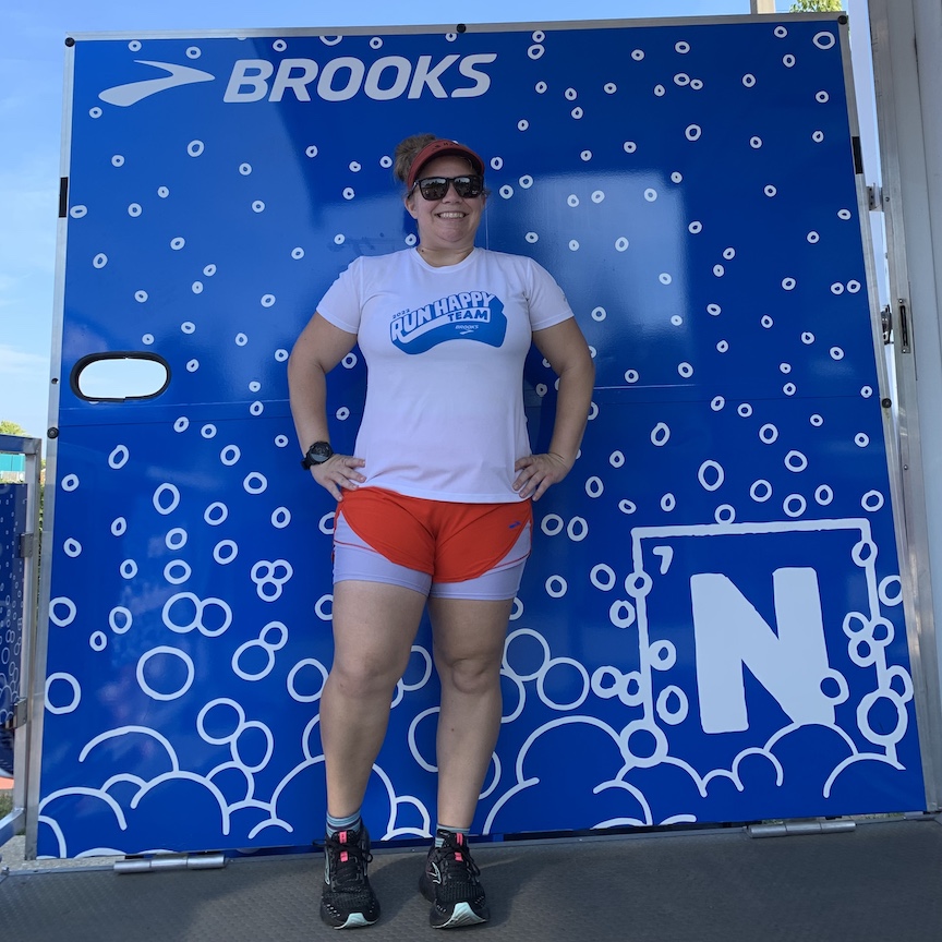 Vanessa Junkin poses in front of a Brooks Run Happy Team backdrop. 