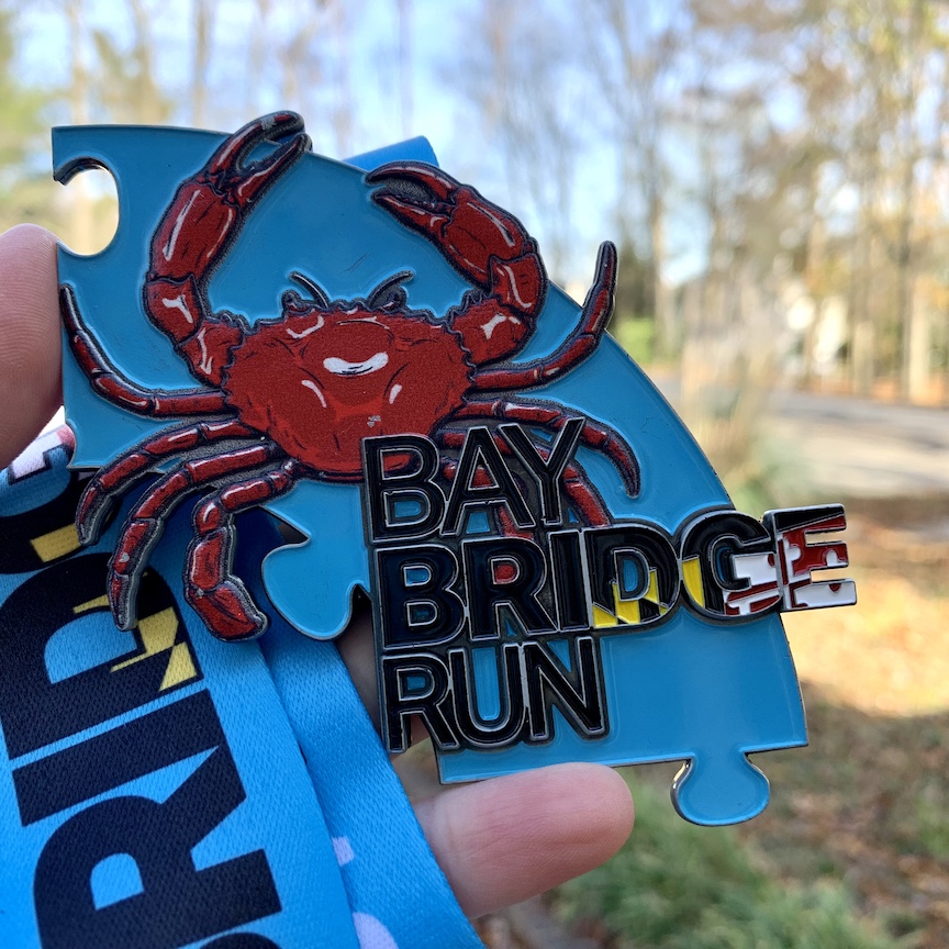 Close-up of the Bay Bridge Run medal, which is blue with a crab and the name of the race on it. 