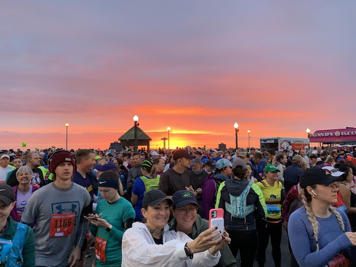 A group of runners, including two runners taking a selfie, with a beautiful sunrise in the background. 