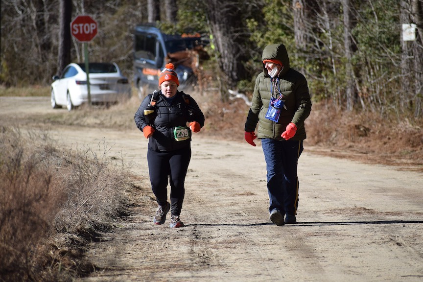 Two female runners on dirt road. One is struggling and the other is supporting. 