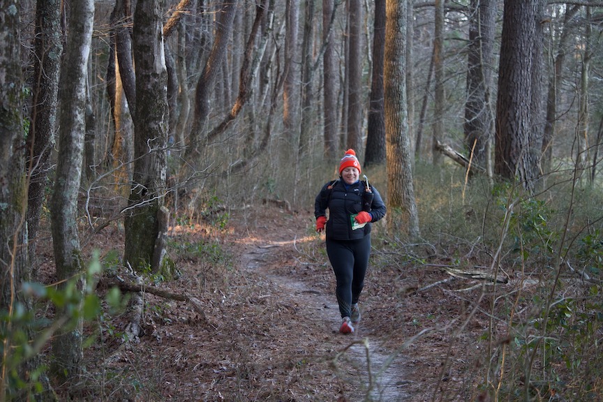 Female runner, bundled up for winter, running on a thin trail. 