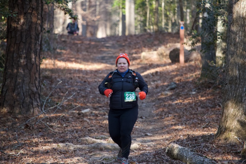 Bundled-up female runner on a trail making a struggling face. 