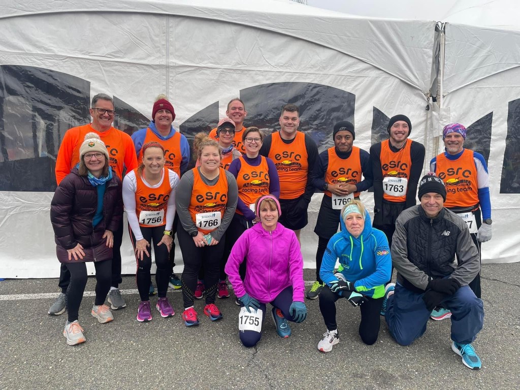 Group photo of 15 runners, with many wearing an orange tank top that says "ESRC Racing Team" with artwork.