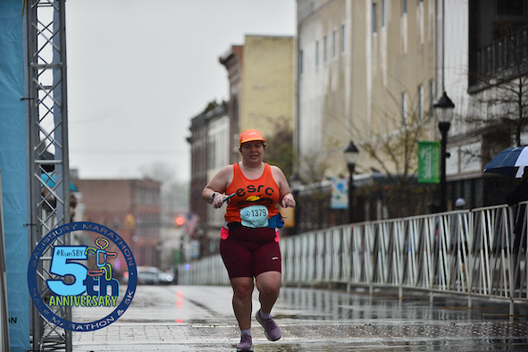 Female runner crosses the finish line of the Salisbury Half Marathon, alone. The road is wet. 