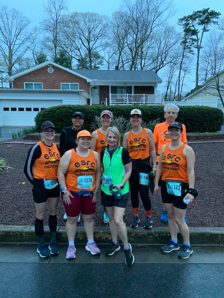 Group of runners pose for a photo, many wearing the same orange team tank. 