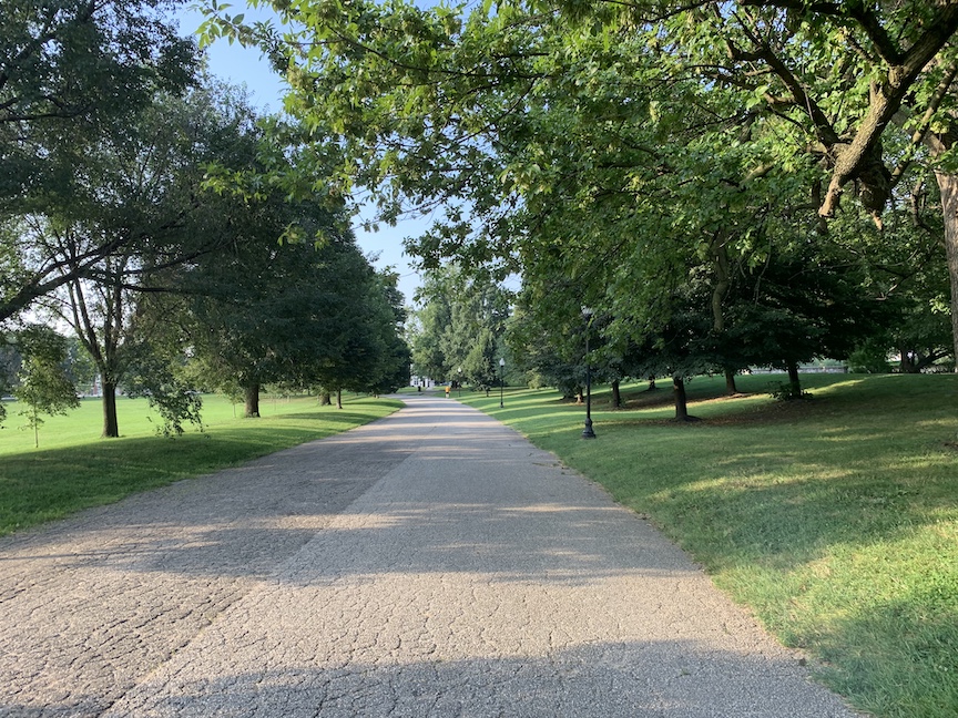 Paved path in Patterson Park with grass and trees to the sides of the path.
