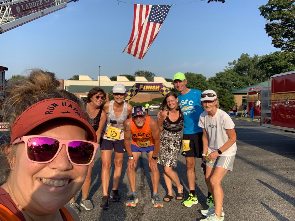 Group of runners in a selfie with an American flag flying in the background. 