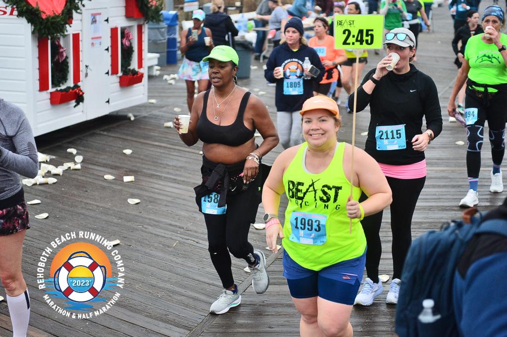 Vanessa Junkin, in bright yellow Beast Pacing tank and holding a sign, smiles for a photo during a running race.