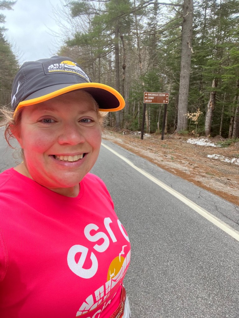 Selfie of Vanessa Junkin with sign that says "Kancamagus Highway" with arrows pointing both ways, and Conway with a left arrow - 12 and Lincoln with a right arrow - 22. 