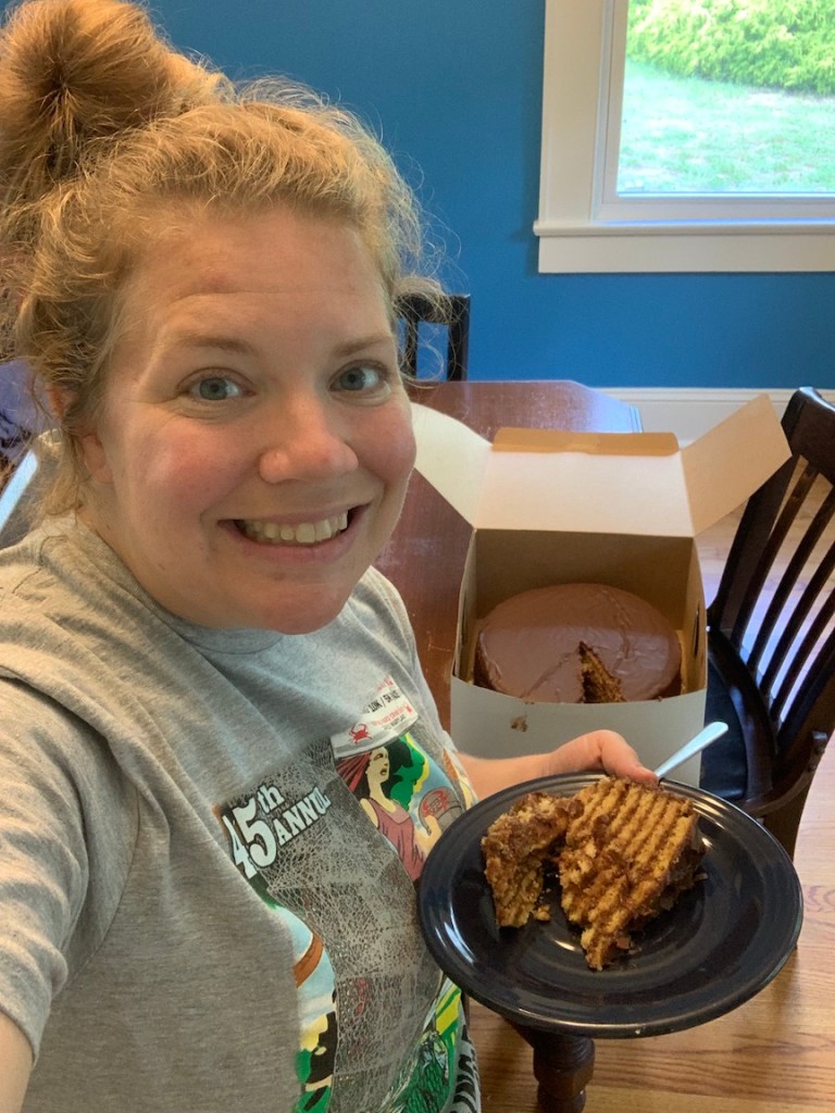 Vanessa Junkin takes a selfie in a gray T-shirt with a piece of Smith Island cake on a plate and the rest of the cake in the background.