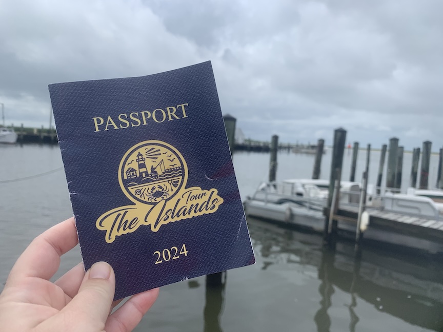 The Islands Tour passport with a marina in the background on an overcast day. 
