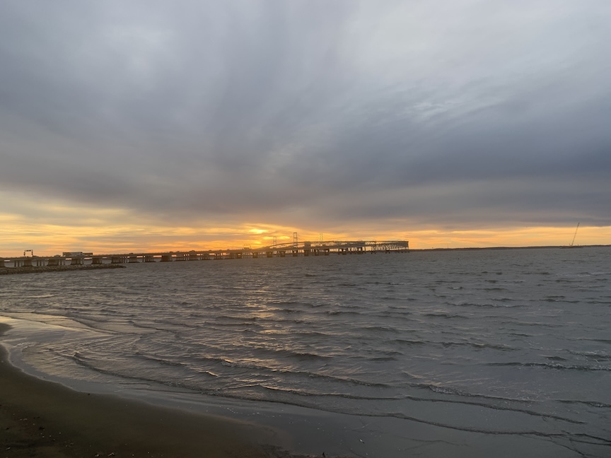 Sunrise over the Bay Bridge, with water in the foreground.