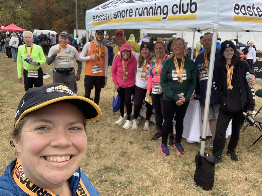 Group of runners smiles for a photo after the race. The photo also shows the Eastern Shore Running Club tent. 