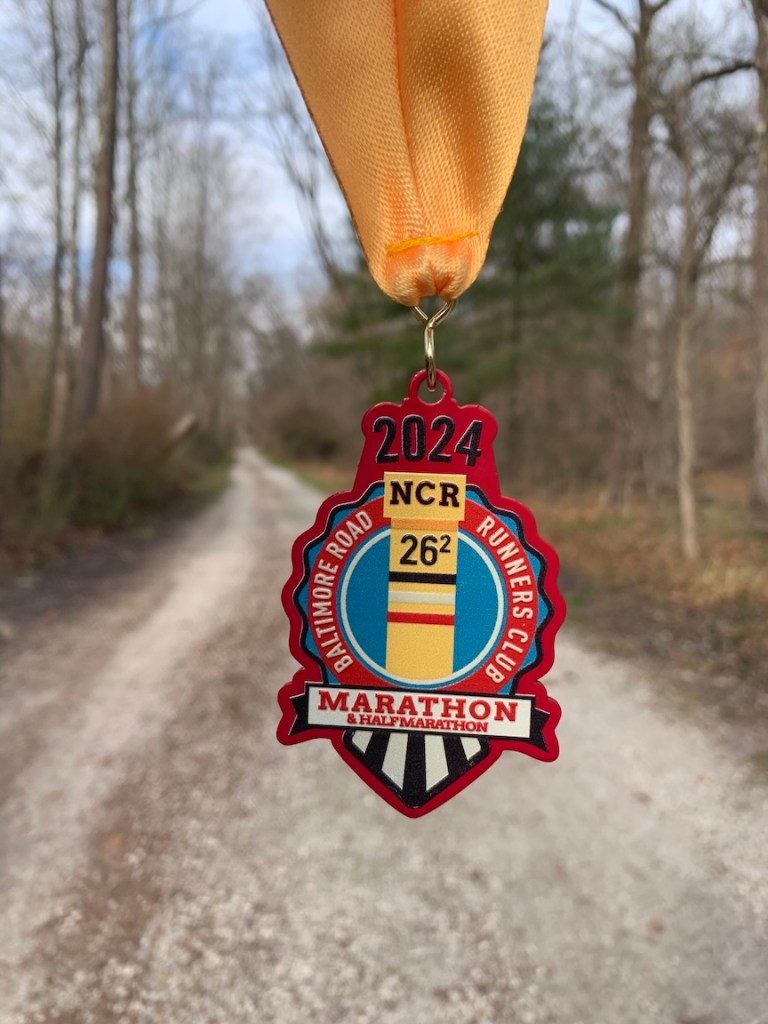 NCR Marathon finisher medal with the trail in the background. 