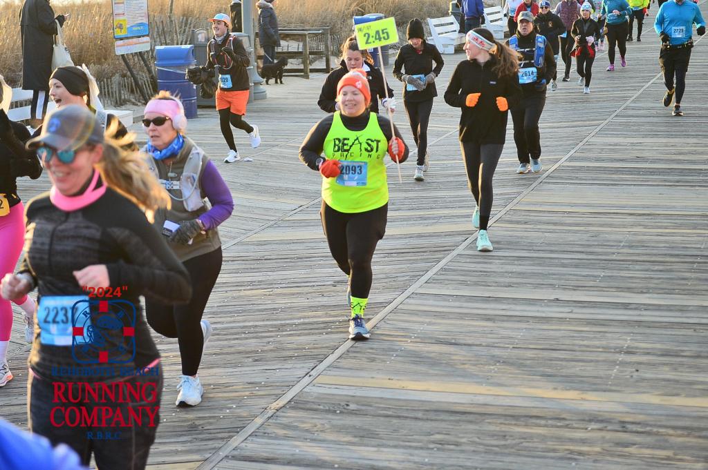 Vanessa Junkin, wearing her Beast Pacing shirt with a black shirt underneath and black pants, holds a 2:45 pace sign during the Rehoboth Seashore Marathon. 