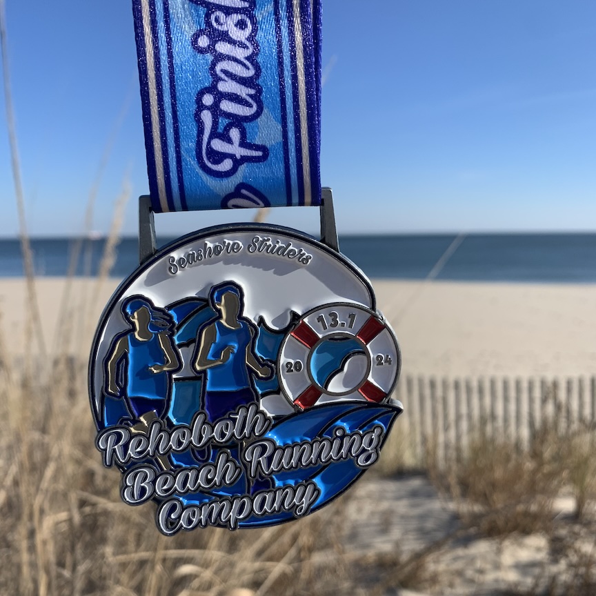 Rehoboth Beach Seashore Half Marathon medal with the beach behind it. 