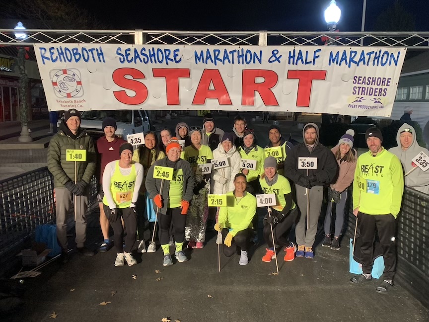 Group photo of Beast Pacing pacers before the Rehoboth Seashore Marathon and Half Marathon under the start banner. 
